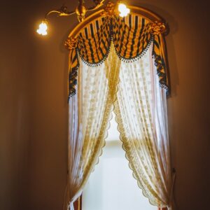 A beautifully styled window with ornate curtains and soft lighting inside a vintage room.