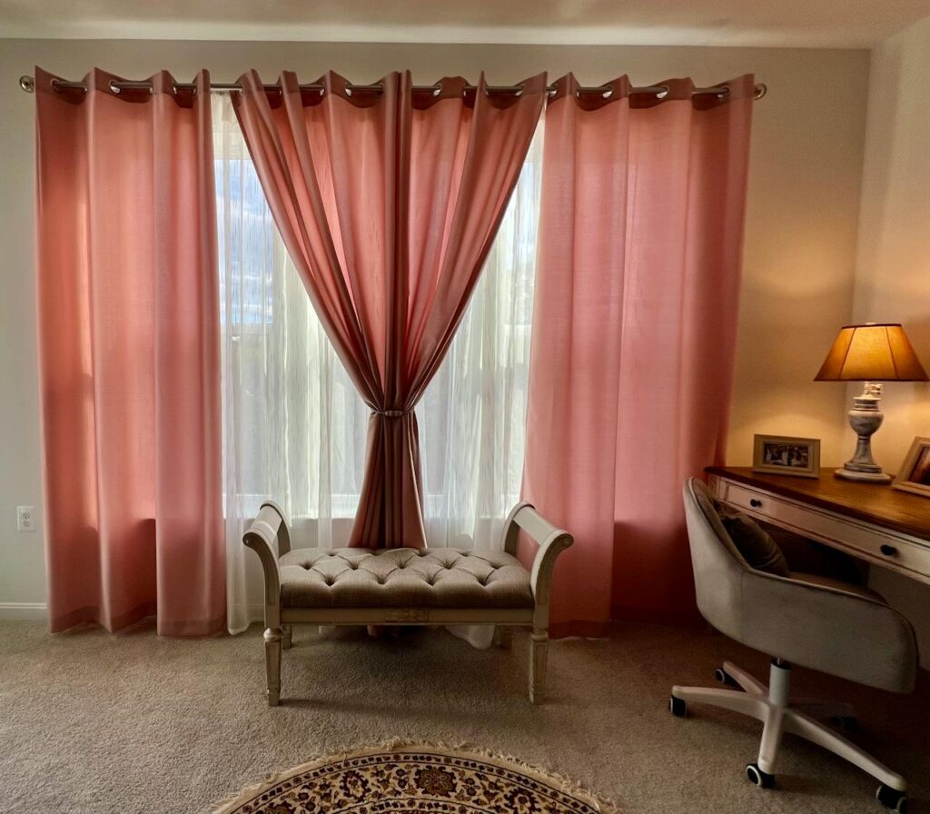 Cozy interior featuring soft pink curtains, a tufted bench, and a stylish desk with lamp.